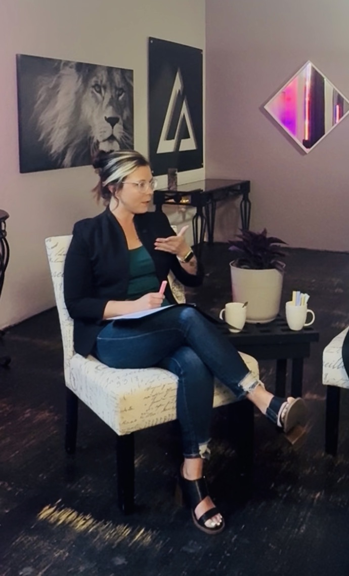 Jenn Resler speaking during a seated discussion, holding notes and gesturing to her audience